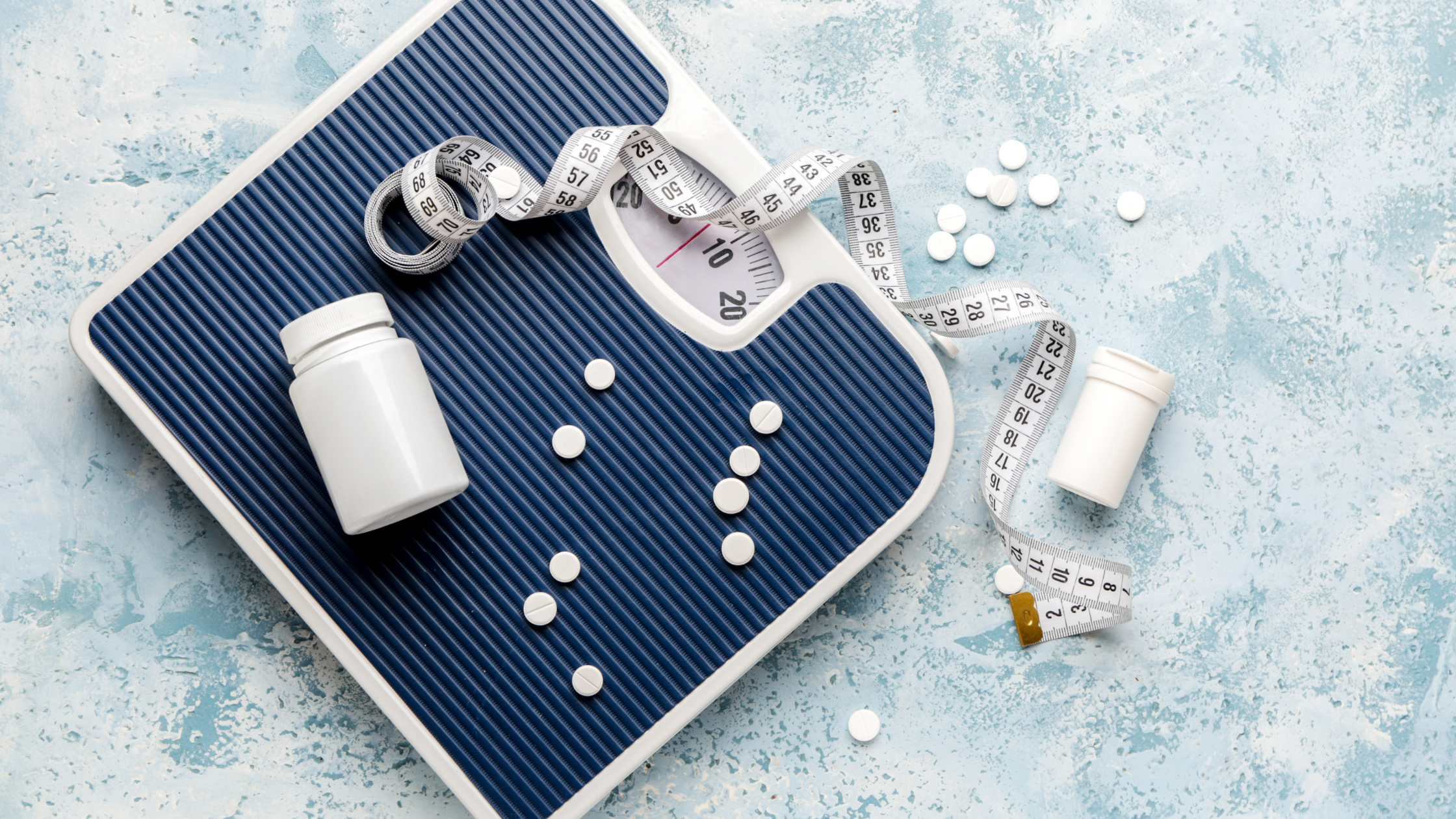 weight loss medication on a scale with a measuring tape